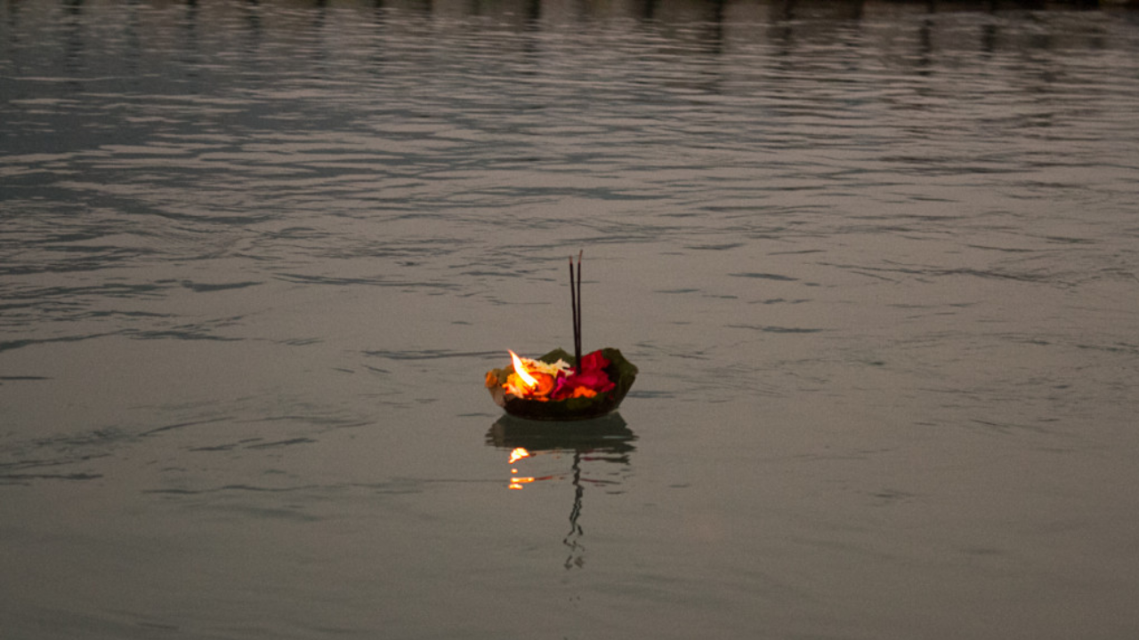 Floating diya lamp offering on the Ganges during the spiritual evening prayer ceremony in Rishikesh with flower petals and candlelight reflecting on the holy river at dusk