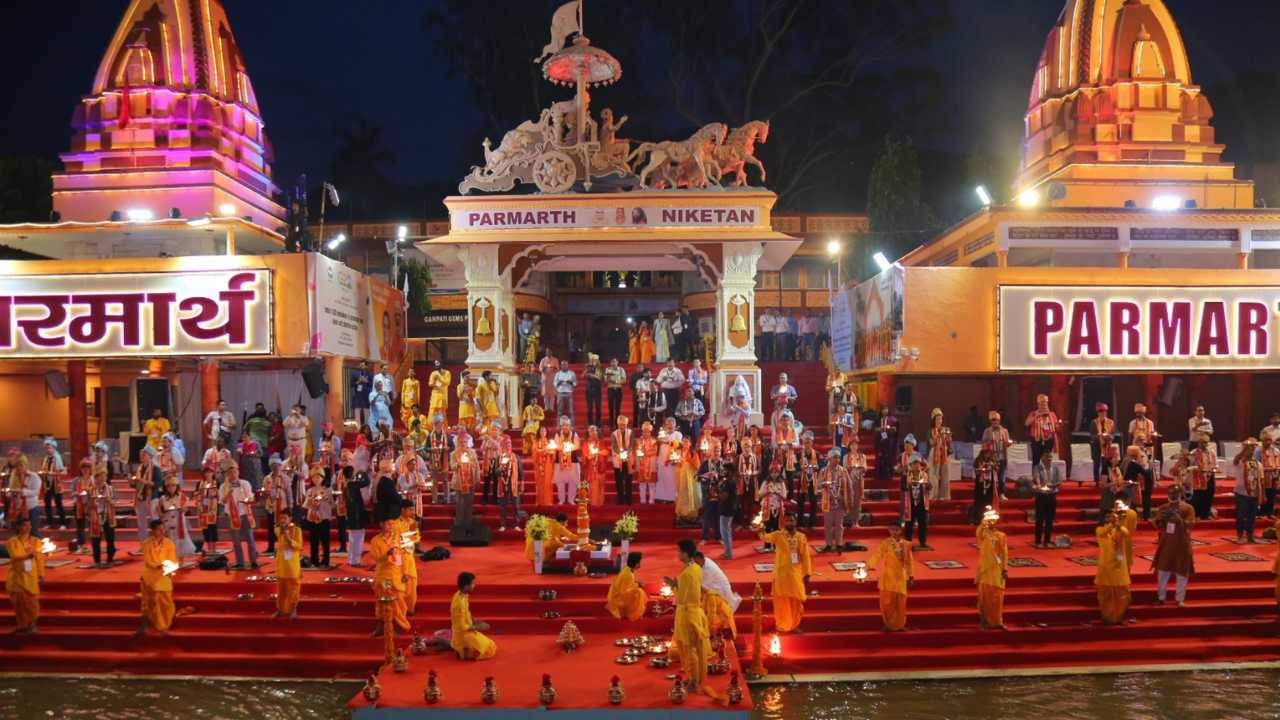 Parmarth Niketan evening prayer ceremony Rishikesh with priests and devotees performing the sacred Ganges ritual beside the flowing river at dusk with oil lamps and flowers