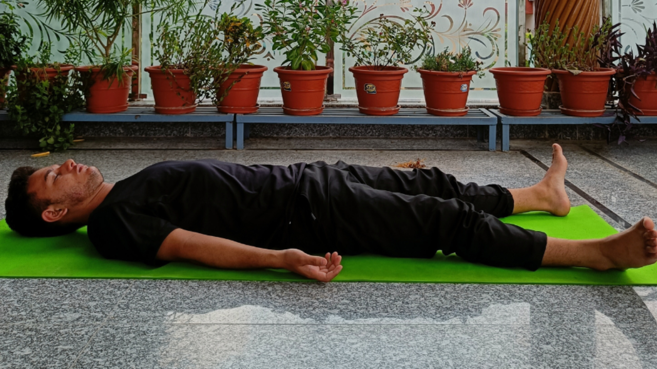 Student in deep Savasana relaxation with eyes closed on yoga mat in peaceful shala