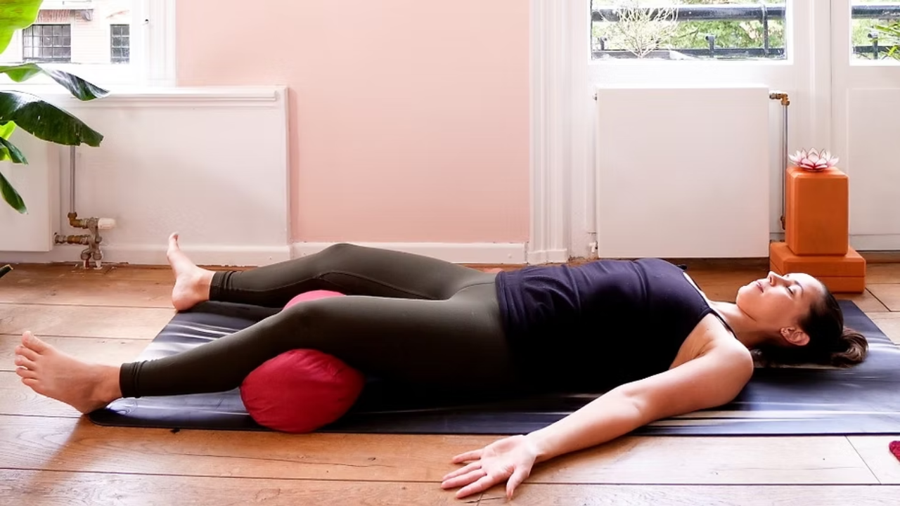 Savasana modification showing bolster placed under knees for lower back support and comfort