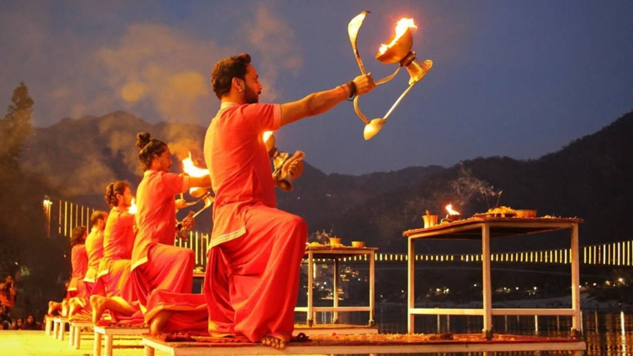 Triveni Ghat Ganga Aarti Rishikesh with priests holding fire lamps during the grand evening sacred river ritual at sunset with large crowd of devotees on the ghat steps