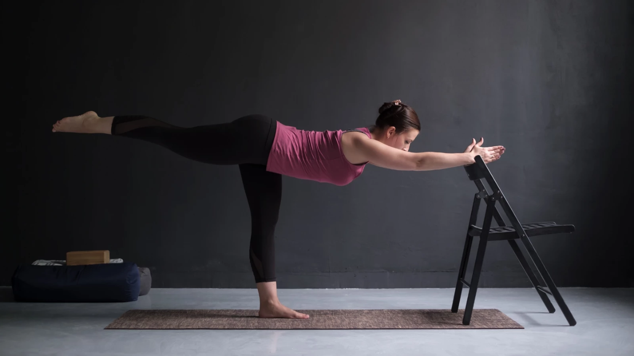 Yoga teacher correcting a student's Warrior III Pose alignment — showing common mistakes like open hip and bent standing leg